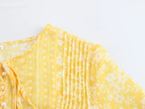 Detail of yellow floral chiffon dress with ruffled shoulders and pearl button accents
