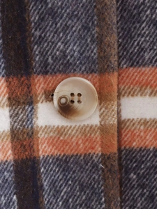 Detailed macro shot of orange plaid wool fabric with a marble pattern button closure
