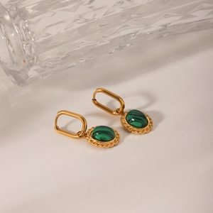 Detailed shot of vintage gold earrings with oval malachite pendants on glass texture