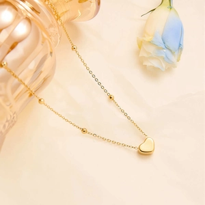 Detailed shot of golden stainless steel heart necklace with beaded chain on soft fabric