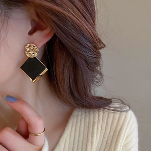 Close-up of geometric gold and black square drop earring worn by a model