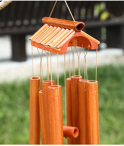 Close-up of natural bamboo wind chime tubes with a wooden roof on a green background