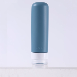 Blue 100ml silicone travel bottle with white cap for toiletries on a white surface