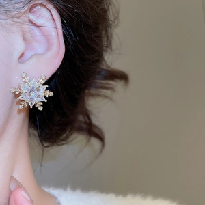 Close-up of elegant gold snowflake stud earrings with zircon crystals worn by a model