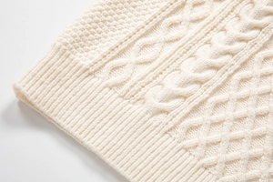 Dettaglio macro del maglione a trecce da uomo con trama bianco crema e polsini a coste