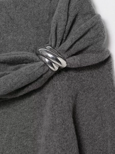 Detail of cross-shaped silver metal buckle on a dark grey knit off-shoulder sweater