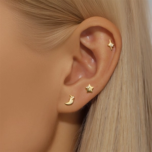 Close-up of gold star and moon stud earrings set with white zircon on ear lobe