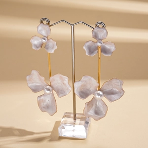 Detail shot of purple flower earrings with gold stems and pearls on a clear stand