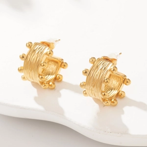 Detail of golden C-shaped metal earrings with draped texture and beaded edges