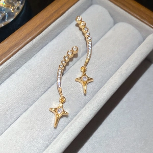 Makroansicht goldener Sternen-Ohrhänger mit funkelnden Zirkonia auf grauem Samtdekor