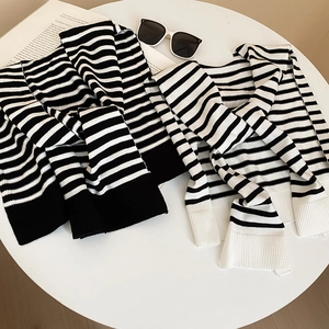 Detailed close-up of striped knit shawl fabric texture and ribbed cuffs on white table