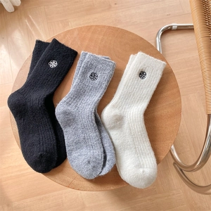 Detail of wool socks in black, grey and white with small floral embroidery and ribbed texture