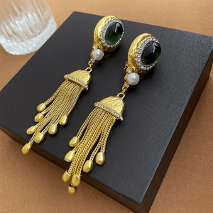 Détail de boucles d'oreilles vintage dorées avec pierres vertes, perles et franges