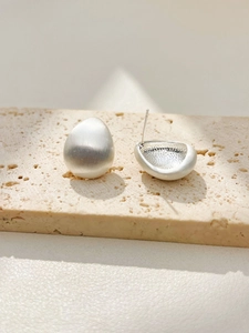 Macro detail of teardrop brushed silver earrings on beige stone showing metallic texture