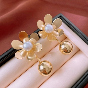 Detail of gold floral earrings with pearl centers and spheres on a red silk background