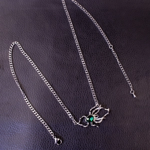 Detailed close-up of a silver spider pendant with a deep green emerald gemstone on black leather