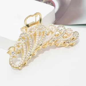 Detail of gold metal hair claw with intricate hollow design, pearls, and rhinestones