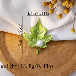 Detailed view of green leaf brooch with pearl on wooden tray showing product dimensions
