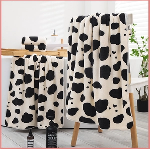 Detailed close-up of cow print coral fleece towel set draped in a modern bathroom setting