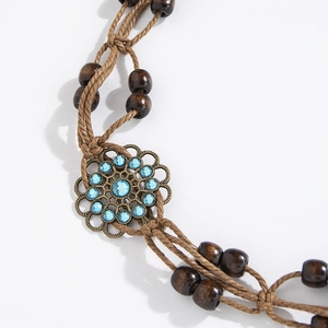 Detail of bohemian braided waist rope featuring dark wood beads and blue rhinestone flower
