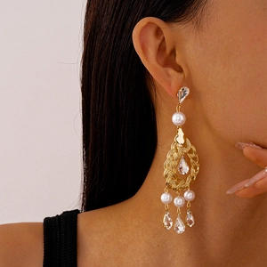 Detail of elegant gold-toned drop tassel earrings with pearls and rhinestones on model