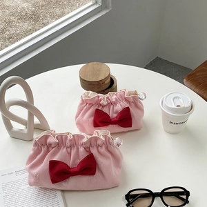 Pink jacquard cosmetic bag with red bow and crystal zipper detail on a white table