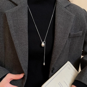 Detail of silver teardrop pendant necklace with long tassel on a grey blazer outfit