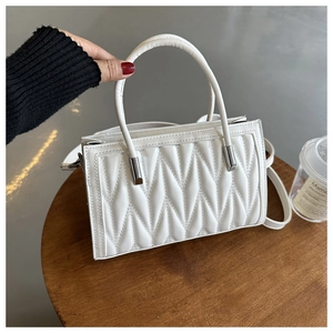 Close-up of white quilted leather handbag with metal handle detail and long shoulder strap