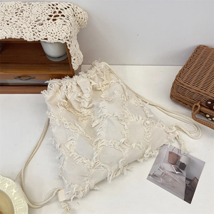Macro detail of bohemian cream drawstring bag featuring textured fringe and woven rope straps