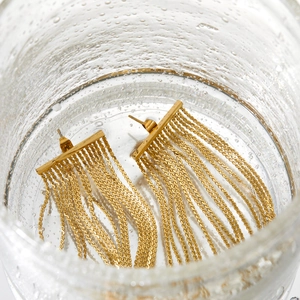 Detailed macro view of gold layered tassel earrings submerged in crystal clear water bubbles