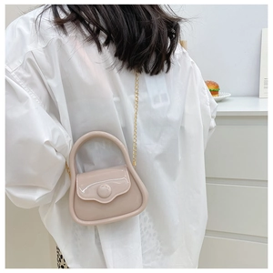 Mini apricot patent leather crossbody bag with gold chain shown on a white shirt model