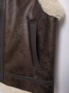 Detail of brown faux leather vest featuring white teddy fleece lining and stitched pockets