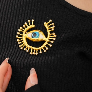 Detailed view of vintage gold eye brooch with blue enamel and rhinestones on black fabric