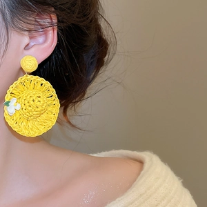 Detail of yellow raffia woven sun hat earrings with small white flower on a female model