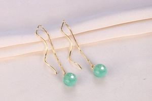 Macro shot of gold tassel earrings with green aventurine jade beads on silk