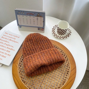 Macro detail of warm orange chunky knit beanie on a rustic wooden tray with cozy decor