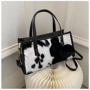 Detail of black and white cow print plush handbag with leather straps and pompom charm