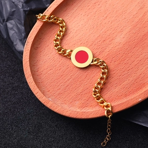 Detail of a gold Cuban link bracelet with a red circular charm on an oval wooden tray