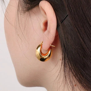 Macro detail of chunky gold U-shaped hoop earring featuring high-polished metal finish
