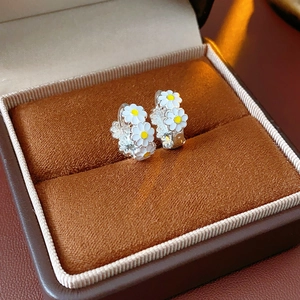 Detail view of silver daisy floral huggie hoop earrings with white and yellow enamel
