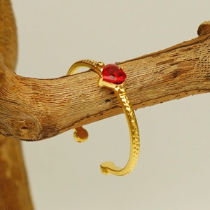Gold open bangle with red heart gemstone and hammered texture on textured wood