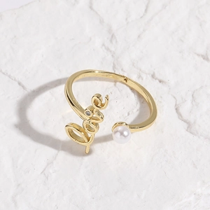 Detail of gold open ring featuring a pearl and Love script on a textured white surface