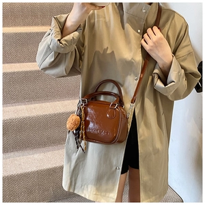 Brown glossy mini square bag with top handle and plush ball charm on a model