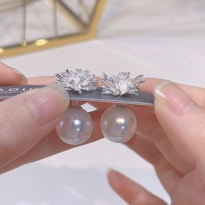 Detail of silver coral-style zircon earrings with a large round lustrous pearl drop