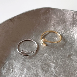 Detailed view of adjustable gold and silver teardrop open rings on a textured plate
