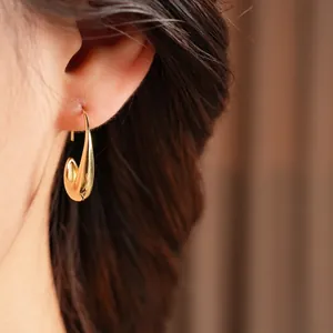 Minimalist 14k gold plated oval drop earrings with mirror finish on female model