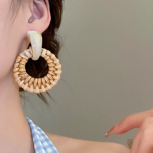 Close-up of handmade round woven rattan earrings with white marble stud on model