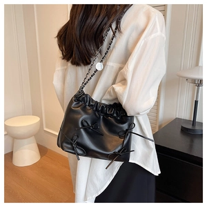 Detail of black pleated bucket bag with bows and chain strap worn by a model
