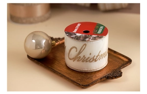 Close-up of white Christmas ribbon with gold glitter text on a festive wooden tray