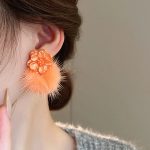 Close-up of orange flower resin earrings with soft pom-pom details on model's ear